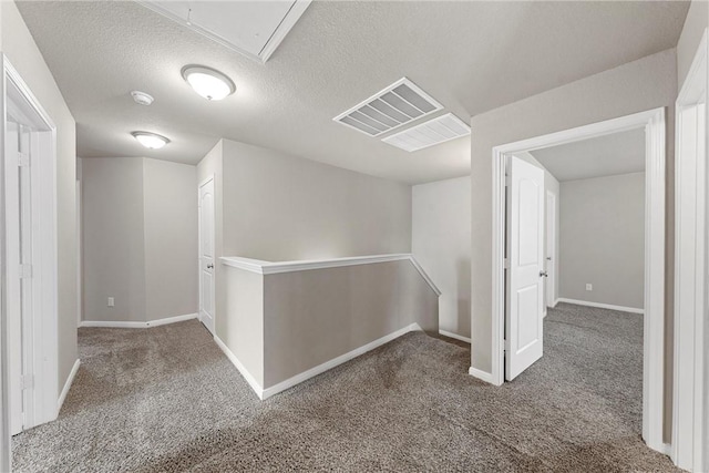 hallway with carpet, visible vents, attic access, a textured ceiling, and an upstairs landing