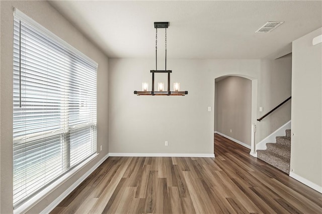 unfurnished dining area featuring arched walkways, visible vents, a wealth of natural light, and wood finished floors