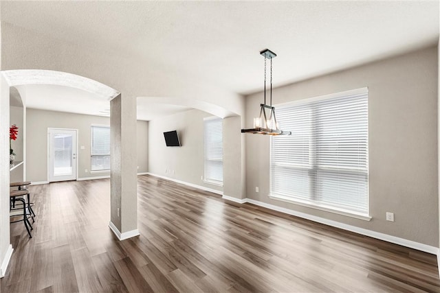 unfurnished dining area featuring baseboards, arched walkways, a chandelier, and dark wood-style flooring