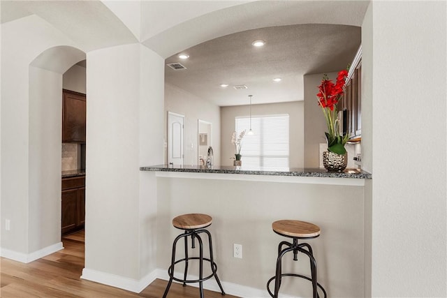 kitchen with visible vents, a breakfast bar, dark stone countertops, light wood-style floors, and arched walkways