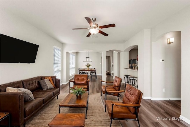 living room with baseboards, arched walkways, wood finished floors, and a ceiling fan