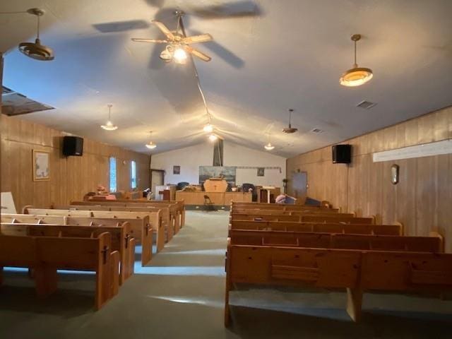 interior space with visible vents, vaulted ceiling, wooden walls, and ceiling fan