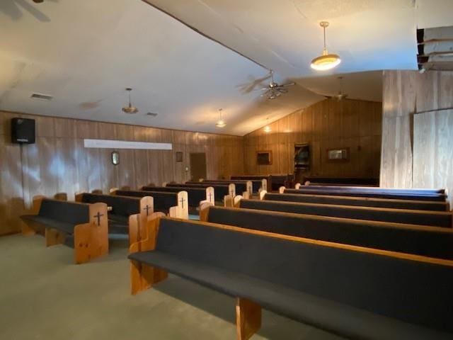 carpeted home theater featuring wooden walls, visible vents, and vaulted ceiling