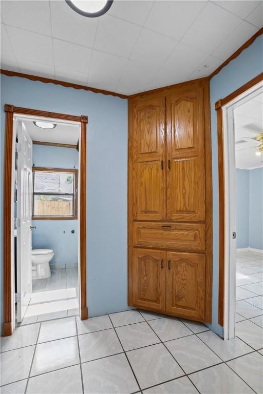 hall with a drop ceiling, light tile patterned floors, and ornamental molding