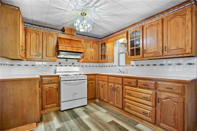 kitchen featuring a notable chandelier, extractor fan, decorative backsplash, white stove, and light wood-type flooring