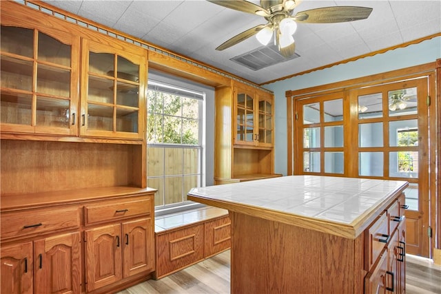 kitchen with ornamental molding, ceiling fan, tile countertops, light hardwood / wood-style flooring, and a center island