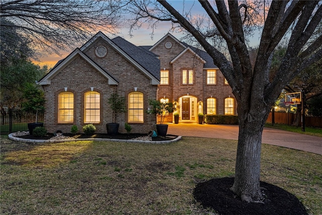 view of front facade with brick siding, a shingled roof, fence, driveway, and a front lawn