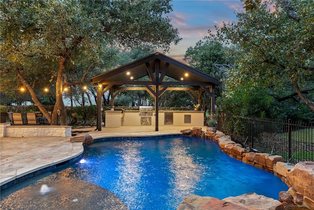 pool at dusk featuring a fenced in pool, a patio, a gazebo, fence, and exterior kitchen