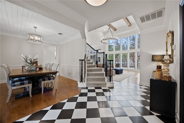 foyer with crown molding, visible vents, a decorative wall, stairway, and a chandelier