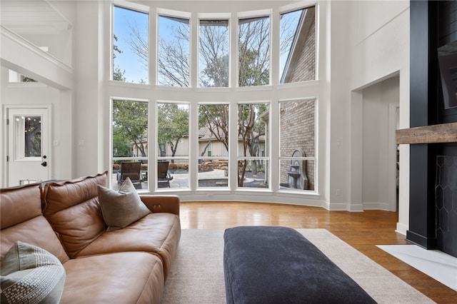 living room featuring a fireplace with flush hearth, wood finished floors, a towering ceiling, and baseboards