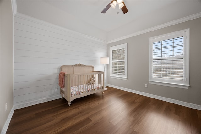 unfurnished bedroom featuring a crib, multiple windows, baseboards, and dark wood-style flooring