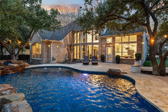 pool at dusk with a patio area and an outdoor pool