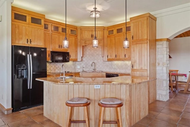 kitchen with tasteful backsplash, light stone counters, an island with sink, and black appliances