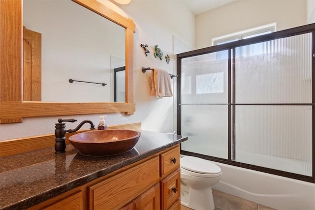 full bathroom with combined bath / shower with glass door, vanity, tile patterned flooring, and toilet