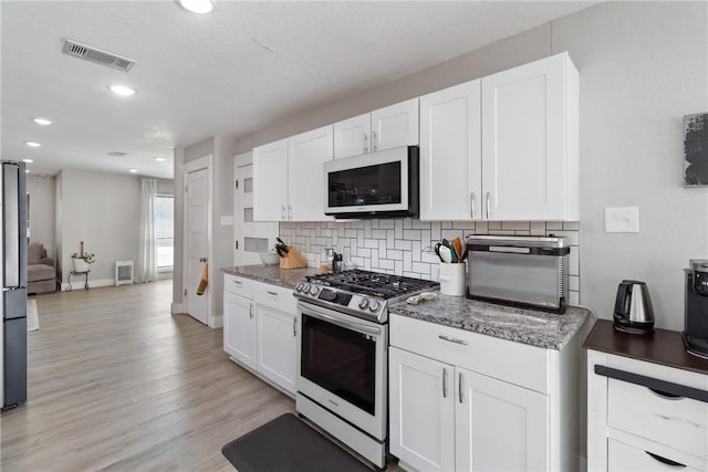 kitchen with white cabinets, light hardwood / wood-style flooring, dark stone countertops, appliances with stainless steel finishes, and tasteful backsplash