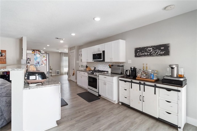 kitchen featuring white cabinets, light hardwood / wood-style flooring, dark stone countertops, tasteful backsplash, and stainless steel appliances