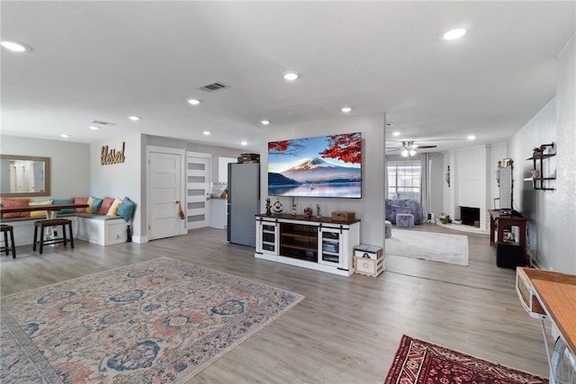 living room featuring ceiling fan, a fireplace, and wood-type flooring