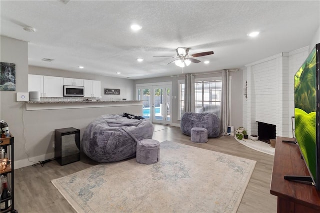 living room featuring a textured ceiling, a fireplace, light hardwood / wood-style flooring, and french doors