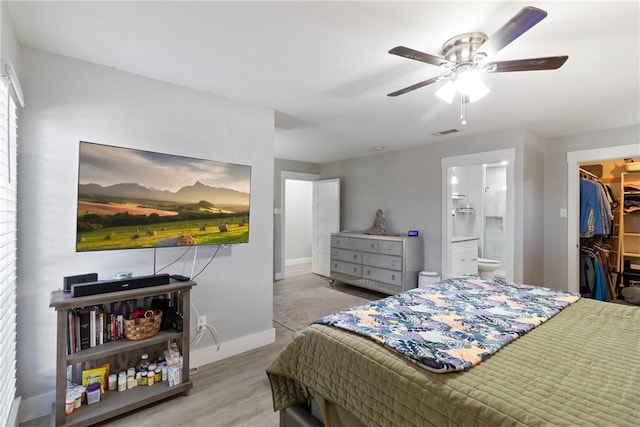 bedroom featuring connected bathroom, a spacious closet, ceiling fan, light hardwood / wood-style flooring, and a closet