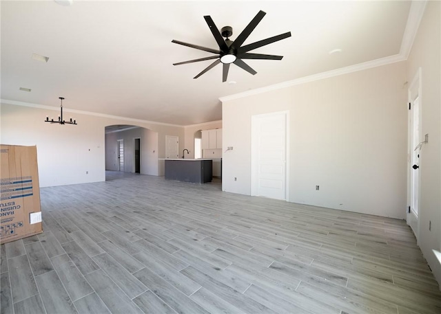 unfurnished living room with ceiling fan with notable chandelier, light wood-type flooring, and ornamental molding