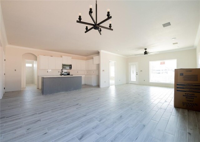 unfurnished living room with ceiling fan with notable chandelier, ornamental molding, and light hardwood / wood-style flooring