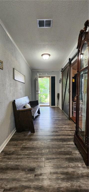 corridor with dark hardwood / wood-style flooring, a barn door, a textured ceiling, and crown molding