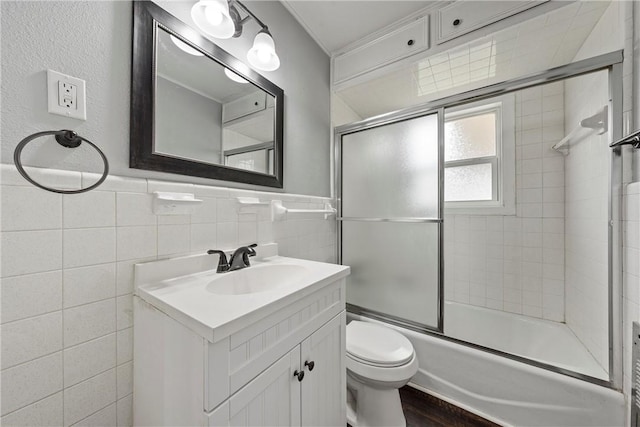 full bathroom featuring toilet, vanity, shower / bath combination with glass door, and tile walls