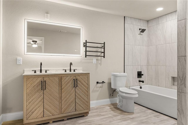 full bathroom with vanity, tiled shower / bath combo, ceiling fan, hardwood / wood-style flooring, and toilet