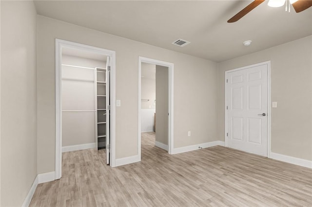 unfurnished bedroom featuring a walk in closet, a closet, light hardwood / wood-style flooring, and ceiling fan