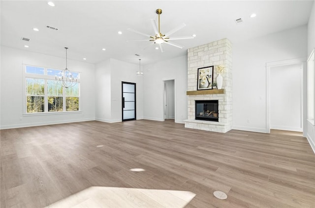 unfurnished living room featuring a fireplace, ceiling fan with notable chandelier, and light hardwood / wood-style flooring