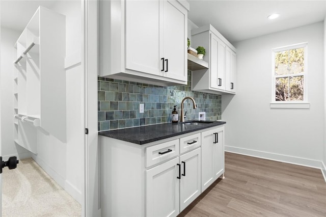 kitchen with sink, dark stone countertops, decorative backsplash, white cabinets, and light wood-type flooring