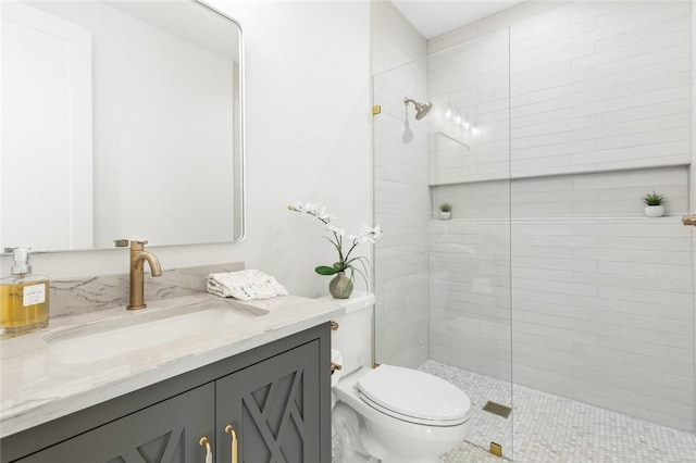 bathroom with a tile shower, vanity, and toilet