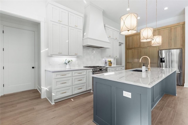 kitchen featuring sink, stainless steel appliances, an island with sink, white cabinets, and custom exhaust hood