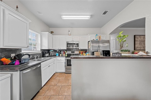 kitchen featuring decorative backsplash, ornamental molding, stainless steel appliances, light tile patterned floors, and white cabinets