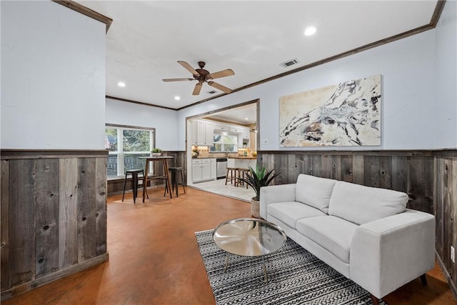 living room with ceiling fan, concrete flooring, crown molding, and wooden walls