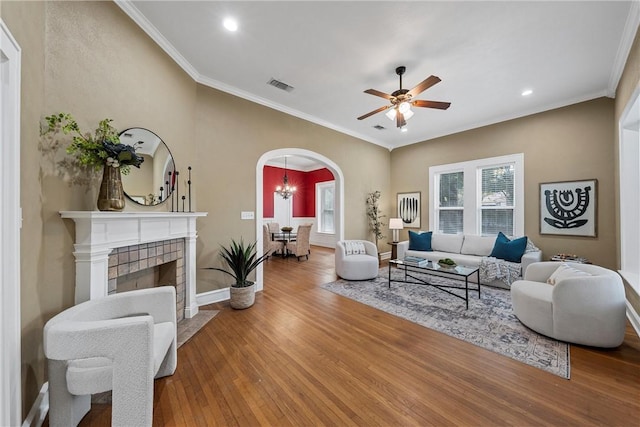 living room with wood-type flooring, ceiling fan with notable chandelier, and ornamental molding