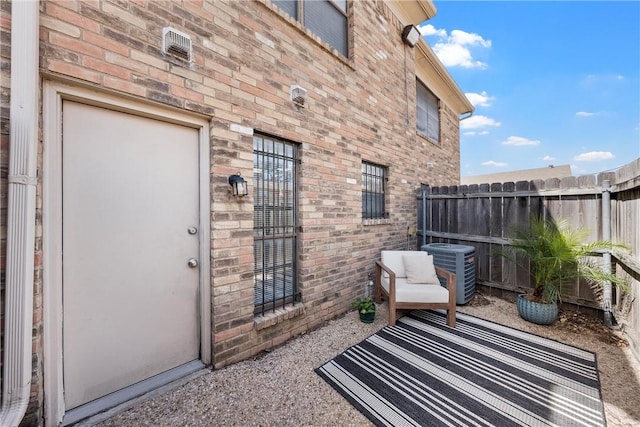 view of exterior entry featuring cooling unit, brick siding, and fence