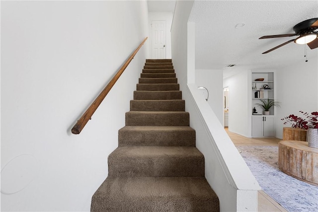 staircase with built in features, visible vents, a textured ceiling, and a ceiling fan