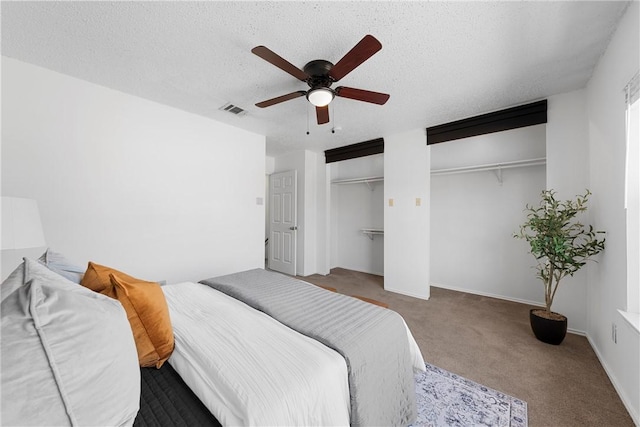 carpeted bedroom with visible vents, multiple closets, a textured ceiling, baseboards, and ceiling fan