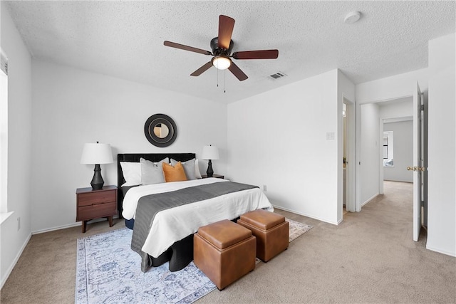 bedroom with a textured ceiling, a ceiling fan, visible vents, and light carpet