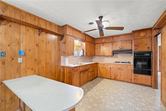 kitchen featuring oven, under cabinet range hood, light countertops, a warming drawer, and a sink