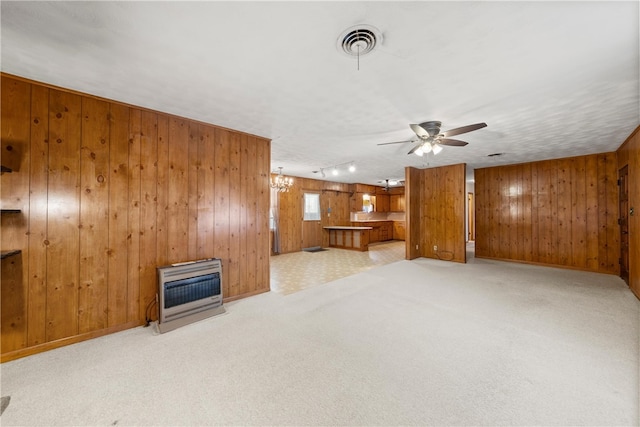 unfurnished living room featuring visible vents, wooden walls, carpet, ceiling fan with notable chandelier, and heating unit