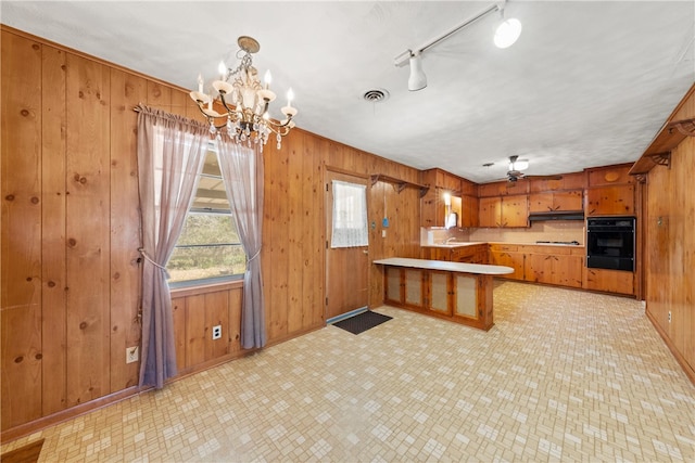 kitchen with visible vents, black oven, under cabinet range hood, brown cabinets, and a peninsula