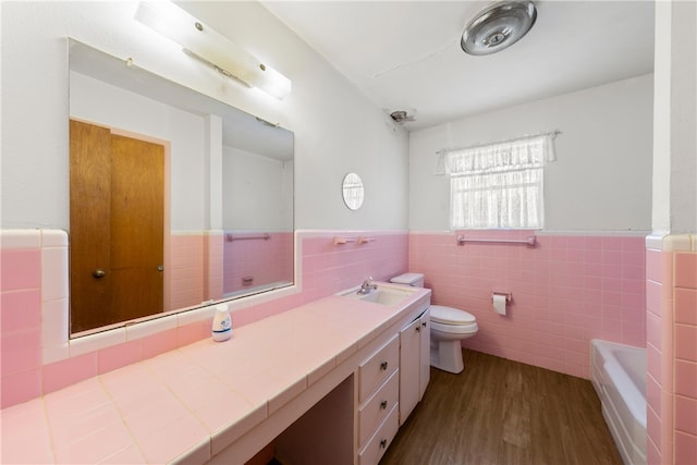 bathroom with vanity, wood finished floors, wainscoting, toilet, and a bathtub