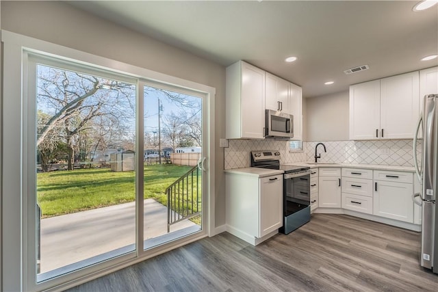 kitchen featuring white cabinetry, light hardwood / wood-style flooring, tasteful backsplash, and appliances with stainless steel finishes