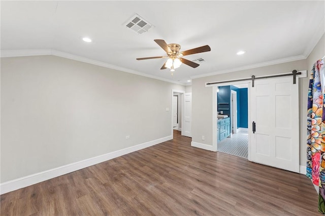 unfurnished bedroom featuring visible vents, a barn door, ornamental molding, wood finished floors, and baseboards