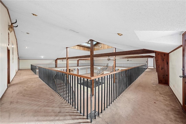 hall with carpet flooring, wood walls, vaulted ceiling with skylight, and a textured ceiling