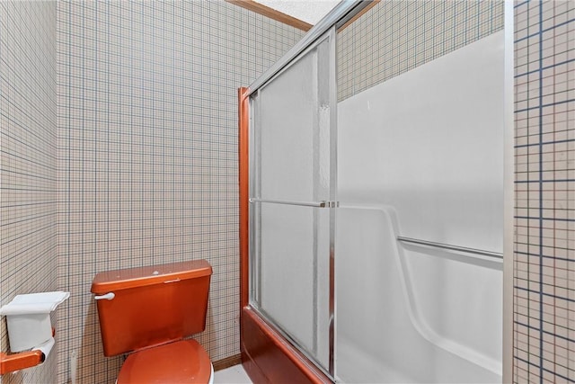 bathroom featuring toilet, tile walls, and enclosed tub / shower combo