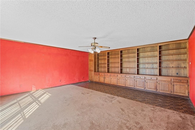 unfurnished living room with ceiling fan, built in features, a textured ceiling, and dark colored carpet