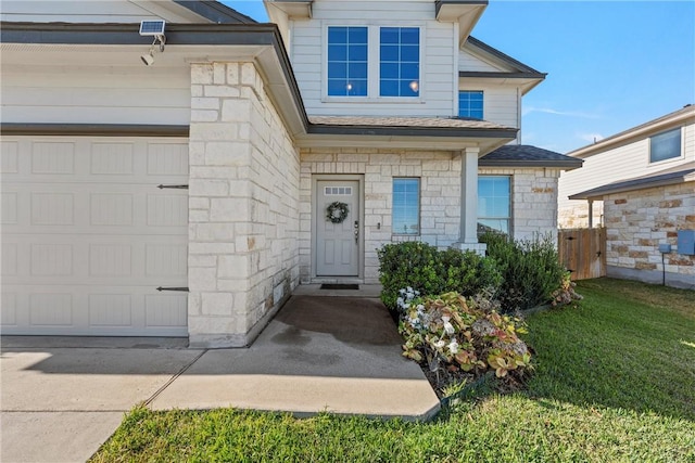 entrance to property featuring a garage, stone siding, a yard, and fence